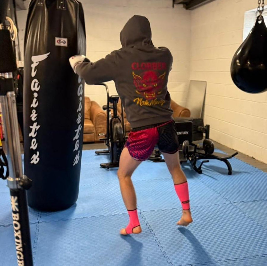Person practicing boxing in a gym with punching bags and exercise equipment.